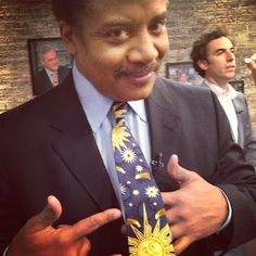 a man in a suit and tie giving the thumbs up sign while another man looks on