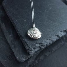 a silver necklace with a shell on it sitting on top of a black stone slab