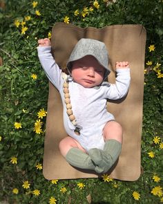 a baby is laying on a mat in the grass with flowers around it and wearing a hat