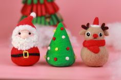 three small christmas ornaments sitting next to each other on a pink surface with trees and decorations in the background