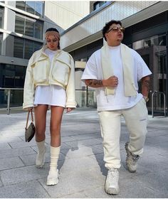 two people walking down the street wearing white clothing and holding hands in each other's pockets