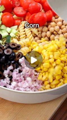 a large bowl filled with different types of vegetables and pasta on top of a wooden table