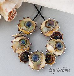 an assortment of beads on a table next to a flower and seashells with pearls