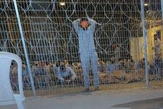 a man standing behind a fence with his hands on his head and arms in the air