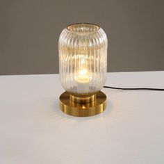 a glass and brass table lamp on a white surface with a black cord plugged in