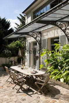 an outdoor dining table and chairs in front of a house