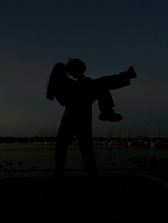 the silhouette of two people holding each other in front of a body of water at night