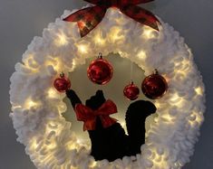 a wreath with lights and ornaments hanging from the front of it, decorated in red and white