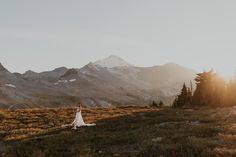 a bride and groom standing in the mountains at sunset