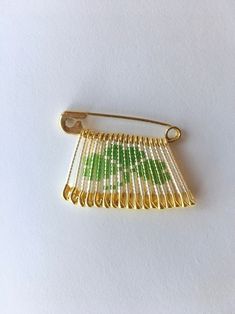 a green and white brooch sitting on top of a white table next to a yellow tie pin