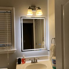 a white bathroom sink sitting under a mirror next to a window with blind shades on it