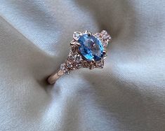 a ring with a blue stone surrounded by smaller stones on a white fabric background in close up view