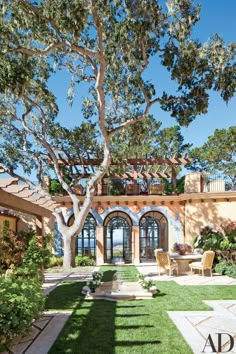 an outdoor patio with chairs and tables under a tree in front of a large house