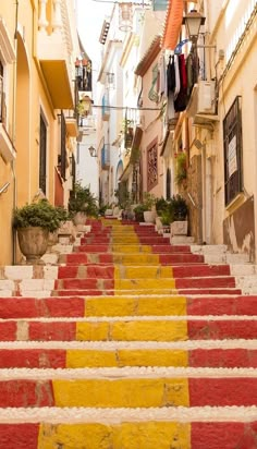 the stairs are painted yellow, red and white in an alleyway with laundry hanging on clothes line above them