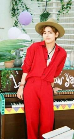 a boy in a red jumpsuit and hat sitting at a piano