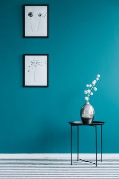 a vase with flowers on a small table in front of a wall painted teal