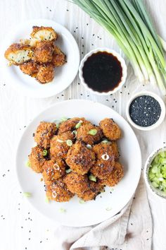 two white plates filled with fried food next to some dipping sauces and green onions