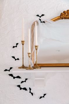 two candles are sitting on a mantle with bats flying around it and a mirror in the background