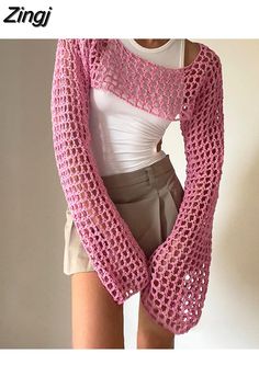 a woman is wearing a pink crocheted sweater and shorts with her hands in her pockets