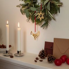 a christmas wreath hanging on the wall next to two candles and an envelope in front of it