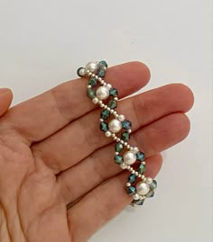 a hand holding a beaded bracelet with pearls and blue glass beads on the end