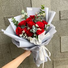 a bouquet of red roses is being held by someone's hand against a brick wall