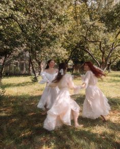 three women in white dresses are walking through the grass