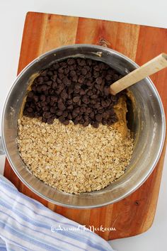 a metal bowl filled with oatmeal and chocolate chips on top of a wooden cutting board