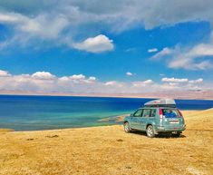 a small car parked on the side of a hill next to an ocean with clouds in the sky