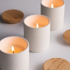 three candles sitting next to each other on top of a white table with wooden coasters