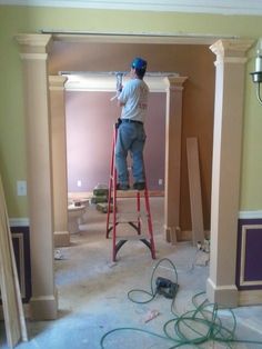 a man standing on a ladder painting the walls in a room that is being remodeled