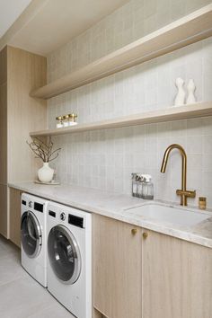 a washer and dryer in a room with white tile on the walls, shelves above