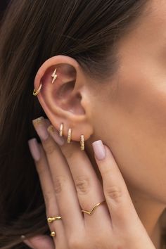 a close up of a woman's ear with three gold rings on her fingers