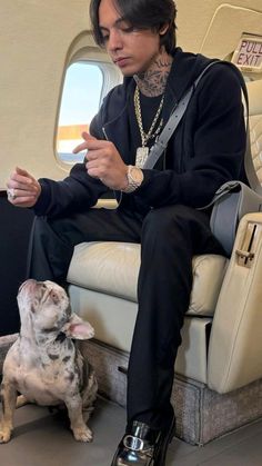 a man sitting on an airplane next to a small dog and looking at his cell phone