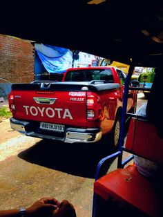 a red toyota truck parked in front of a brick building next to a person sitting on a bench