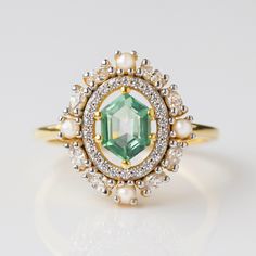 Adorned with an exquisite fern green topaz, this statement ring is set amidst a dazzling CZ and iridescent pearl halo for a radiant finish. Elegant and exclusive, this angelic design exudes class and sophistication - a must-have for any luxury jewelry lover. Non Traditional Vintage Engagement Rings, Unique Gemstone Ring, Angelic Design, Pearl Halo Ring, Green Engagement Rings, Pearl Halo, Hexagon Engagement Ring, Gem Rings, Pearl Wedding Ring