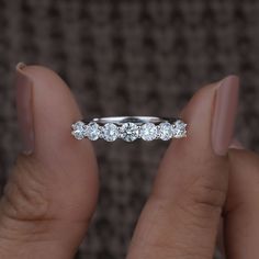 a woman's hand holding a wedding band with five diamonds on top of it