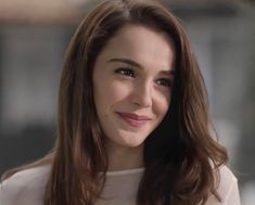 a close up of a person wearing a white shirt and smiling at the camera with long hair