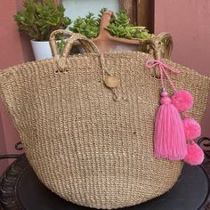 a large straw bag with pink tassels and a keychain hanging from it