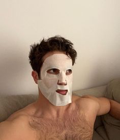 a shirtless man with a sheet mask on his face is laying on a couch