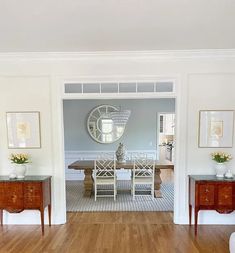 an open door leading to a dining room and living room with wood floors, white walls and wooden furniture