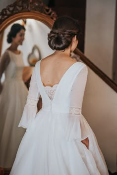 a woman standing in front of a mirror wearing a wedding dress