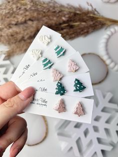 someone is holding up some small christmas tree studs on their earring postcards