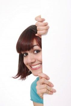 a woman is peeking out from behind a white board with her hand on the edge