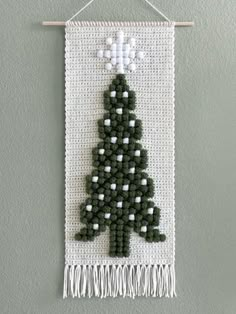 a cross stitch christmas tree hanging on a wall with white and green trimmings