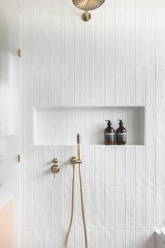 a white tiled bathroom with two shower heads and soap dispensers on the wall