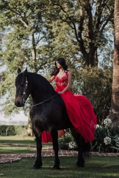 a woman in a red dress is sitting on a black horse and posing for the camera