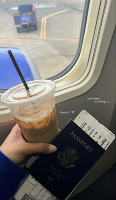 a person holding a passport and a drink in front of an airplane window with the door open