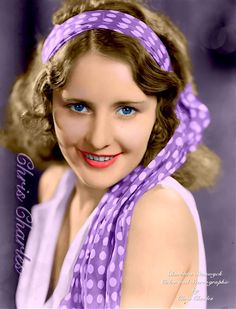 a woman with blue eyes and a purple scarf around her neck is smiling at the camera