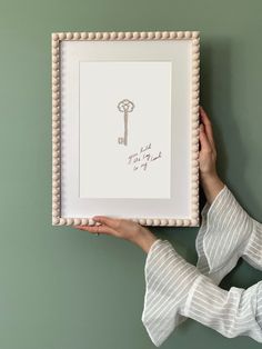 a woman holding up a framed artwork with a key